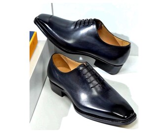 May include: A pair of dark navy blue leather oxford shoes with a polished finish, featuring a square toe design, a low stacked heel, and thin black laces. The shoes have a tan interior lining and a structured silhouette with clean stitching.