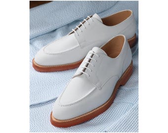 May include: A pair of white leather dress shoes with a classic design. The shoes have a light brown sole and white laces. The shoes are displayed on a light blue textured fabric.