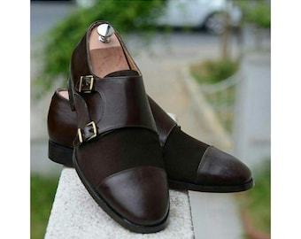 May include: A pair of dark brown double monk strap shoes featuring a smooth leather toe cap, a suede vamp, and two gold-toned metal buckles on the side. The shoes are equipped with wooden shoe trees inserted inside to maintain their shape.