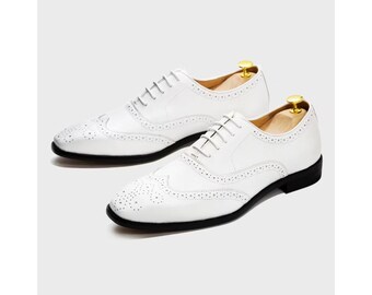 May include: A pair of white leather Oxford shoes with decorative perforations and black soles. The shoes have a classic wingtip design and are laced up with white laces. The shoe trees are visible inside the shoes.