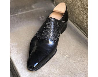 May include: A black leather oxford shoe featuring a polished toe cap and a textured, pebbled leather vamp. The shoe includes thin dark laces, a row of decorative perforations along the seam, and a light-colored wooden shoe tree inserted inside.