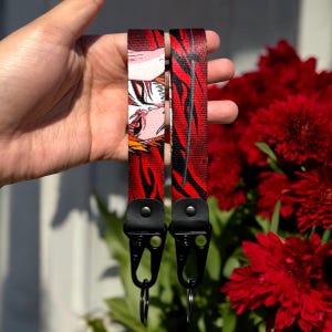 May include: Two red and black patterned keychains with black metal clips and rings. The keychain features an anime character with red and white hair.