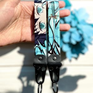 May include: Two blue and black anime character lanyards with black metal clasps and key rings. The lanyards feature a blue and white background with a black and white anime character.