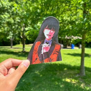 May include: A red and black anime character with long black hair and red eyes is holding her hands together in front of her. She is wearing a red jacket with black trim and a white shirt. The character is smiling with a mischievous expression.
