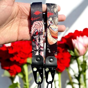 May include: Two black and red anime character printed lanyards with black metal clips. The lanyards feature a black and white background with red accents.