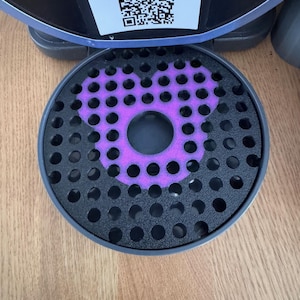 Peut inclure: Un couvercle de bac d'égouttage noir circulaire pour machine à café avec une découpe en forme de tête de Mickey Mouse violette. Au-dessus se trouve une étiquette blanche avec un QR code et le texte SCAN BELOW TO GET STARTED. POUR LA MEILLEURE BARBOTINE.