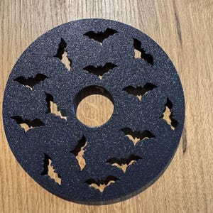 Op de afbeelding: Een donkerblauwe, ronde onderzetter met een glitterafwerking. De onderzetter heeft vleermuisuitsparingen rond de rand en een centraal gat. De onderzetter is waarschijnlijk gemaakt van een duurzaam materiaal.