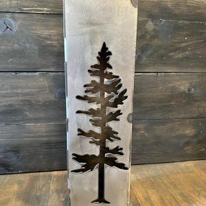 May include: A metal log holder with a cut-out design of a pine tree. The holder is a rectangular shape with a square base.