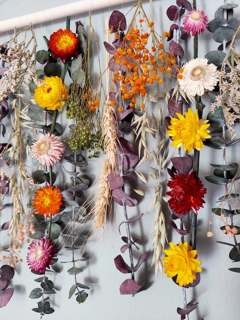 May include: A dried flower wall hanging with a variety of colors and textures, including yellow, orange, red, pink, and white. The flowers are arranged in a cascading pattern and are interspersed with dried grasses and eucalyptus leaves.