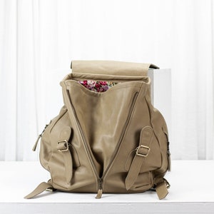 May include: A tan leather backpack with a floral lining. The backpack has two large zippered compartments and two smaller zippered pockets on the front.