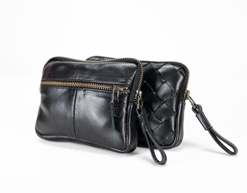 May include: A black leather zippered pouch with a woven leather design. The pouch has a small strap and a zippered pocket on the front.