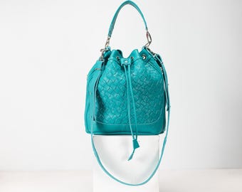 May include: A teal blue woven leather bucket bag with a drawstring closure and a long shoulder strap.