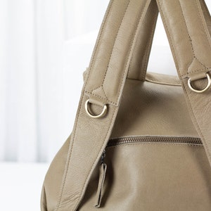May include: A tan leather backpack with two adjustable straps and gold metal hardware. The straps have a quilted design.