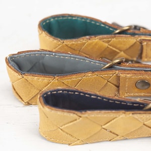 Op de afbeelding: Drie geweven leren banden met verschillende gekleurde voeringen. De banden zijn lichtbruin van kleur en hebben een geweven patroon. De voering is groen, grijs en donkerblauw.