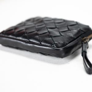 May include: A black leather woven wallet with a zipper closure and a small pull tab.