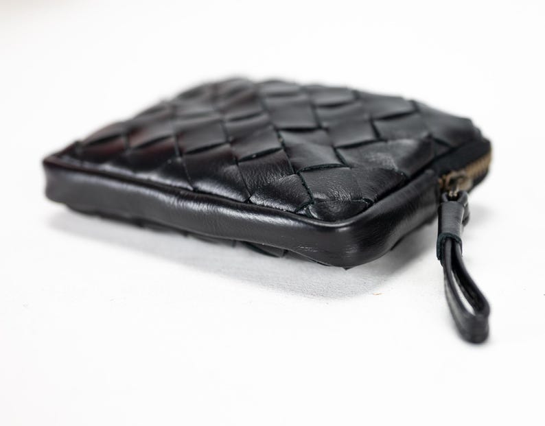 May include: A black leather woven wallet with a zipper closure and a small pull tab.
