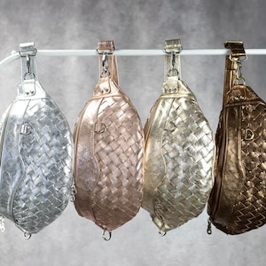 May include: Four woven leather sling bags in silver, rose gold, gold, and bronze. Each bag has a zippered closure and a shoulder strap. The bags are hanging from a white metal bar against a gray background.