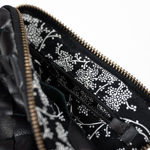 May include: A black leather woven zippered pouch with a black and white floral lining. The zipper is gold colored.