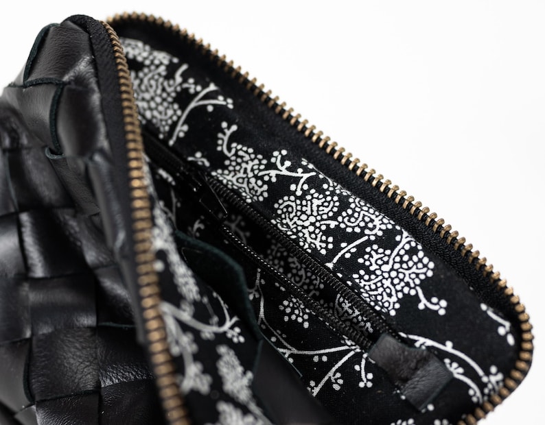 May include: A black leather woven zippered pouch with a black and white floral lining. The zipper is gold colored.