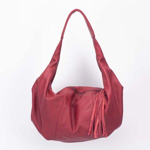 K&ouml;nnte beinhalten: Burgunderfarbene Hobo-Tasche aus Leder mit langem Riemen und Quasten. Die Tasche hat einen Rei&szlig;verschluss und ein weiches, l&auml;ssiges Design. Die Tasche ist aus glattem, geschmeidigem Leder gefertigt.