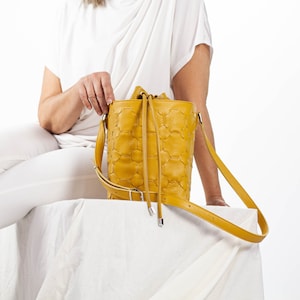 May include: A yellow leather bucket bag with a drawstring closure and a long strap. The bag has a quilted pattern.