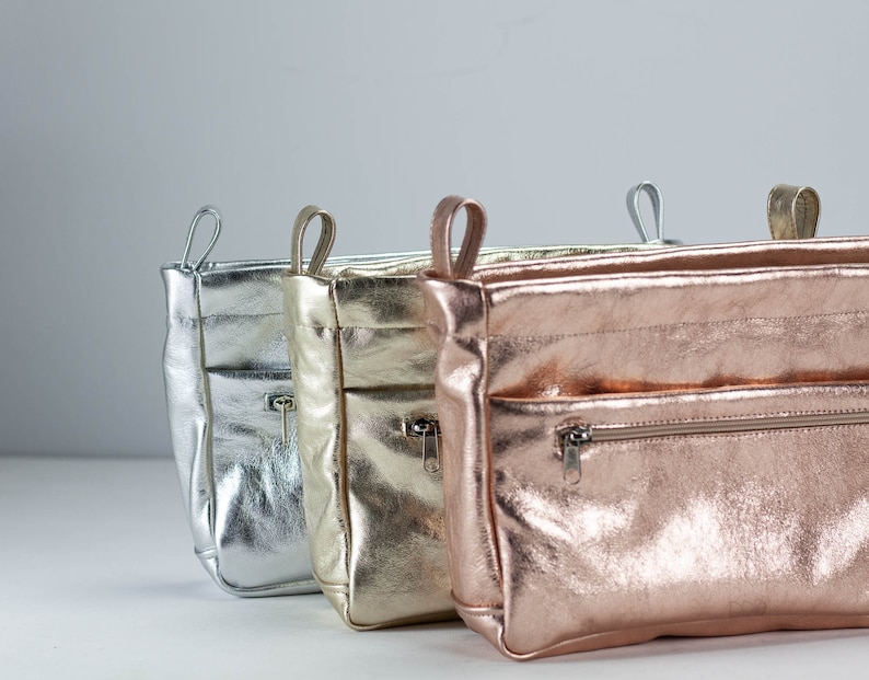 以下が含まれることがあります： シルバー、ゴールド、ローズゴールドのメタリックレザー製のジッパー付きポーチ3つ。ポーチは左から右に並んでいます。