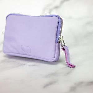 May include: A small lavender zippered pouch with a pink zipper pull. The pouch has a subtle embossed logo on the front.
