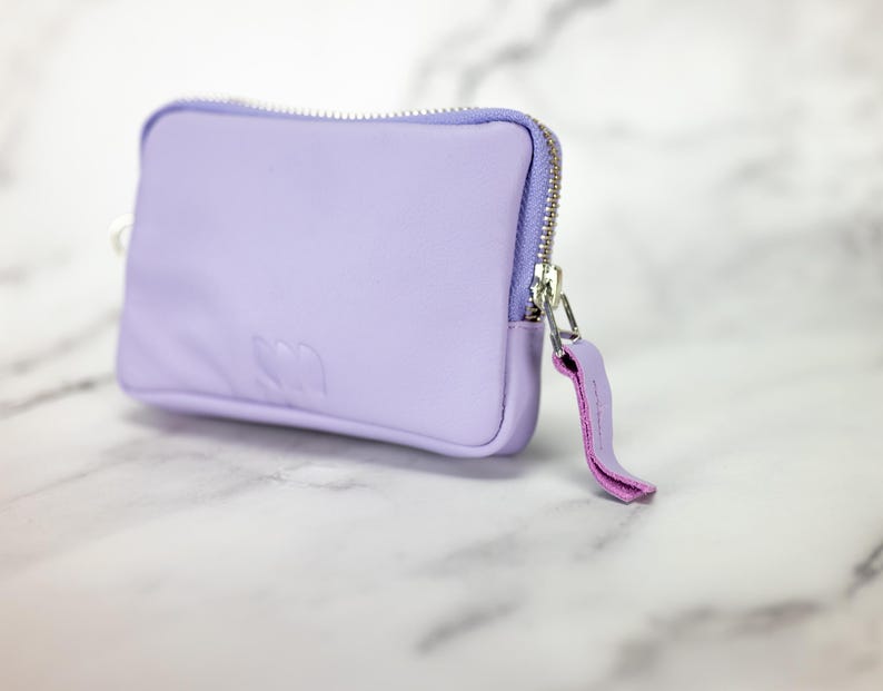 May include: A small lavender zippered pouch with a pink zipper pull. The pouch has a subtle embossed logo on the front.
