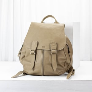 May include: A tan leather backpack with two adjustable straps and a zipper closure. The backpack has a flap with two buckles.