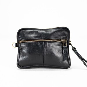 May include: A black leather zippered pouch with a small strap. The pouch has a front pocket and a zipper closure.