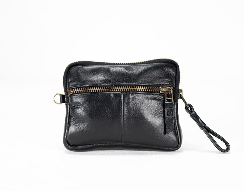May include: A black leather zippered pouch with a small strap. The pouch has a front pocket and a zipper closure.