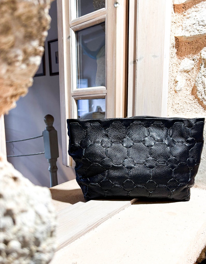 May include: A black leather tote bag with a geometric pattern. The bag is sitting on a wooden surface.