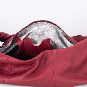 K&ouml;nnte beinhalten: Offene rote Lederhandtasche mit Rei&szlig;verschluss. Das Innenfutter ist ein grauer Stoff mit wei&szlig;em Blumenmuster. Eine kleine Tasche ist im Inneren der Tasche sichtbar.