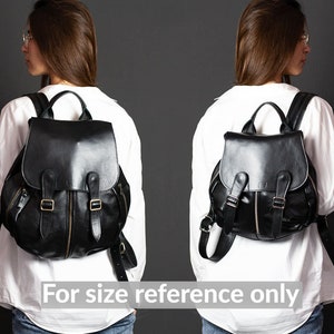 May include: Two black leather backpacks with gold buckles and zippers. The backpacks are worn by two people, but only the backpacks are visible in the image.  For size reference only.