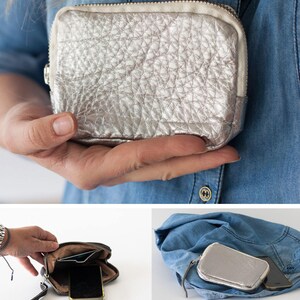 May include: A silver leather zippered pouch with a textured surface. The pouch is open and shows a black phone and a credit card inside.