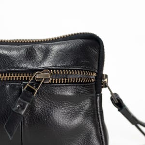 May include: A black leather zippered pouch with a gold zipper. The pouch has a flap with a zipper pull.