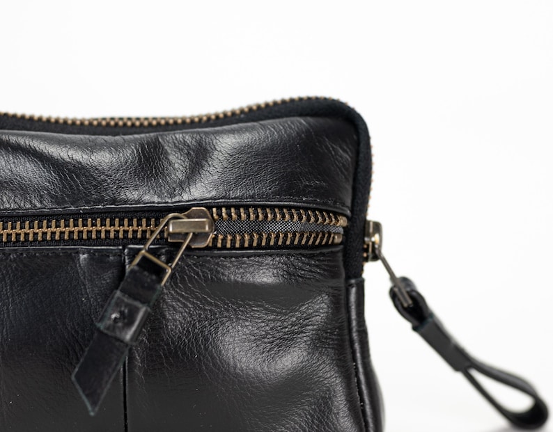 May include: A black leather zippered pouch with a gold zipper. The pouch has a flap with a zipper pull.