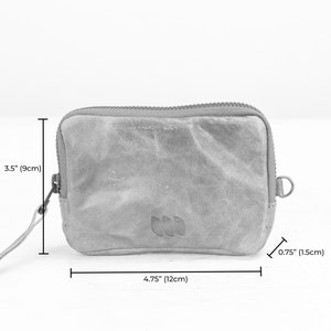 May include: A small, gray, zippered pouch with a leather-like texture. It measures 4.75 inches wide by 3.5 inches tall and has a small loop on the side.