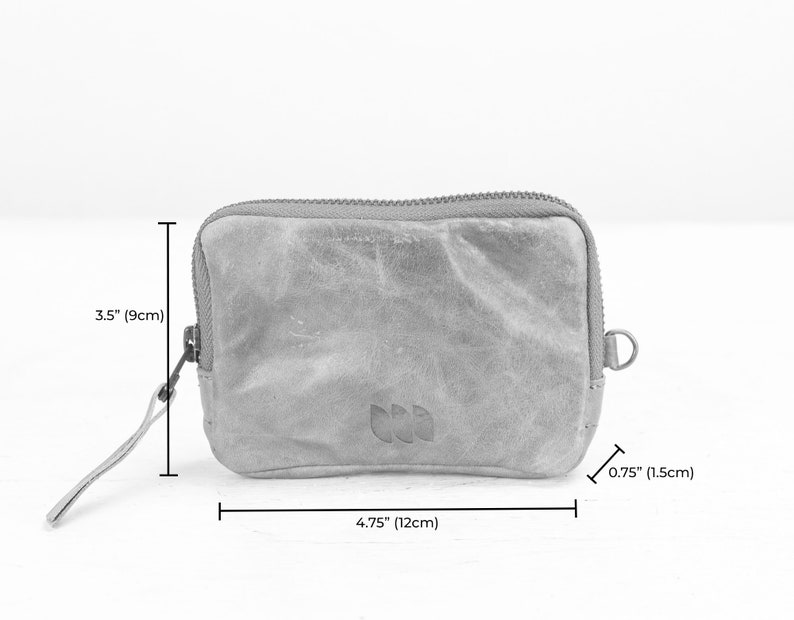 May include: A small, gray, zippered pouch with a leather-like texture. It measures 4.75 inches wide by 3.5 inches tall and has a small loop on the side.