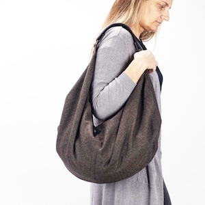 May include: A large, brown shoulder bag with a curved, crescent shape. The bag is made of a textured fabric and has a black strap. The bag is being carried over the shoulder.
