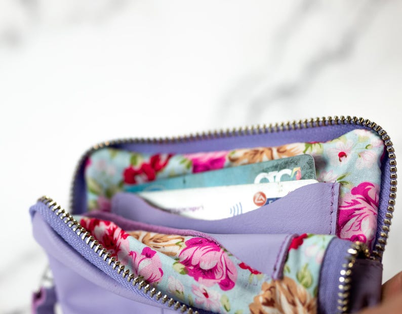 May include: A lavender zippered wallet with a floral lining. The wallet is open and has several cards inside.