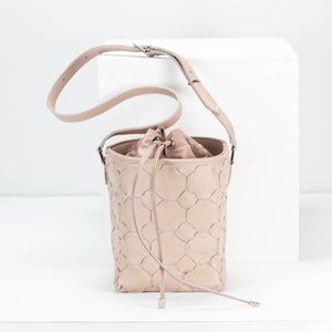 May include: A pale pink leather bucket bag with a drawstring closure and a long strap. The bag has a geometric pattern.