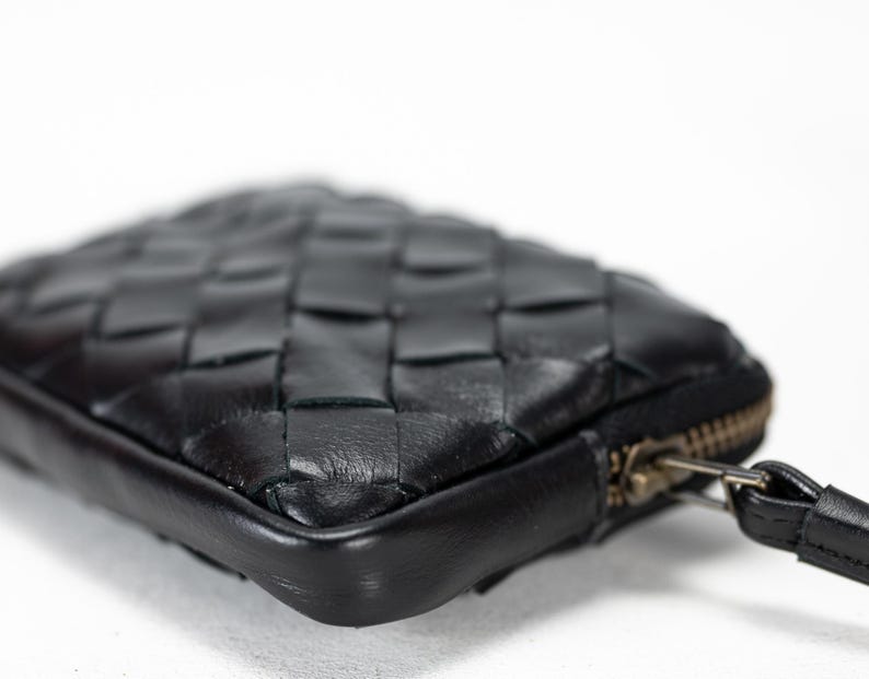 May include: A black leather woven clutch with a zipper closure and a wrist strap.