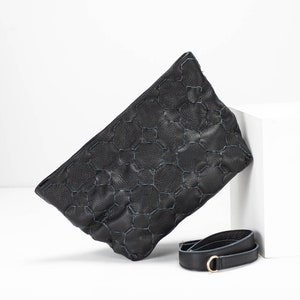 May include: Black leather clutch bag with a geometric pattern and a detachable strap.