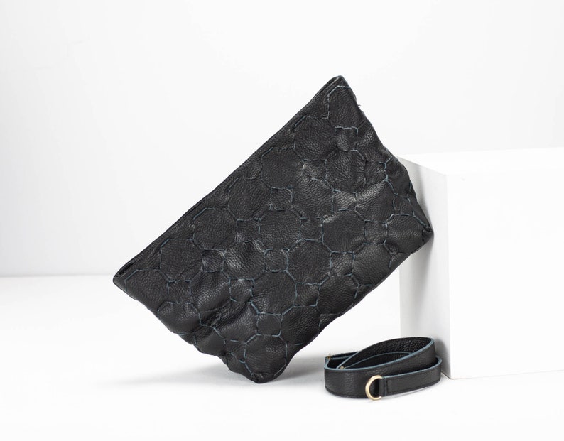 May include: Black leather clutch bag with a geometric pattern and a detachable strap.