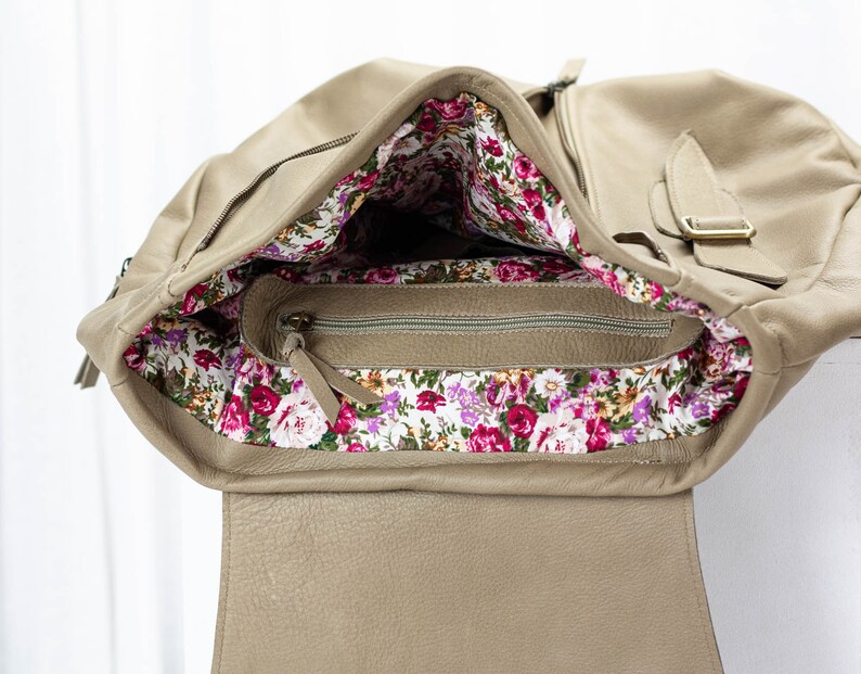 May include: A beige leather bag with a floral lining. The bag has a zipper closure and a flap with a buckle.