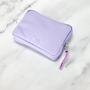 May include: A small lavender zippered pouch with a silver zipper and a pink zipper pull. The pouch has a subtle embossed design.