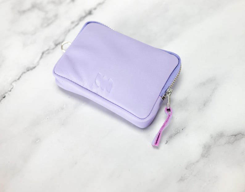 May include: A small lavender zippered pouch with a silver zipper and a pink zipper pull. The pouch has a subtle embossed design.