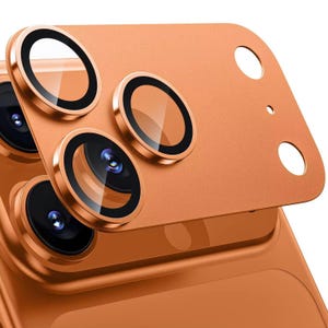 May include: Close-up of a copper-colored phone camera lens protector. The protector has three circular lens covers with black rings and clear glass, and a rectangular base with two circular holes.