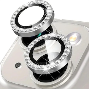 May include: Two silver camera lens protectors with a clear center and a ring of rhinestones around the edge. The protectors are on a white phone.